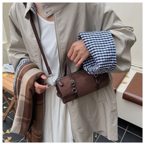 Detail of a brown cylindrical crossbody bag in matte suede with metal buckle accents