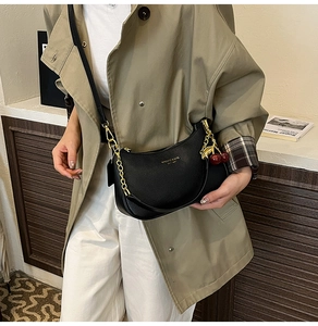 Détail du sac hobo en cuir grainé noir avec chaîne dorée et breloque cerise rouge