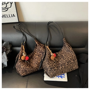 Close-up of leopard print tote bags with fuzzy pom-pom charms on a black leather sofa