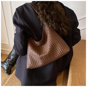 Detail of a dark brown woven shoulder bag with brand label on a striped blazer