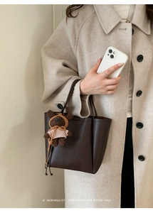 Detail of dark brown pebble leather bucket bag with cute plush bear charm accessory