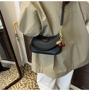 Detail of black pebbled leather crescent bag with gold chain and cherry charm