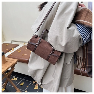 Detail of dark brown suede cylinder bag with silver buckles and leather trim on model