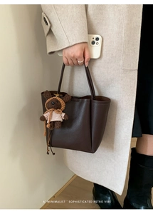 Detail of dark brown lychee leather tote bag with a cute bear plush charm attached
