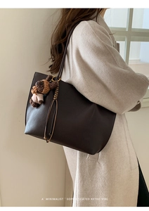 Detail of dark brown lychee leather tote bag with cute bear charm for minimalist styling