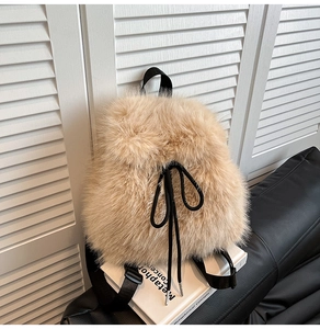 Close-up of beige plush backpack with black drawstring bow and nylon straps on a sofa