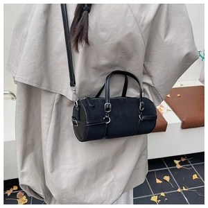 Detailed view of a black cylinder Boston bag worn crossbody over a classic beige trench coat