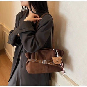 Détail du sac fourre-tout en daim marron avec ceintures à oeillets et breloque ourson