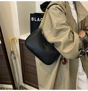 Detail of black lychee grain hobo bag with gold chain and logo worn with a khaki trench coat