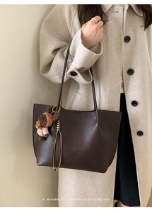 Detail of dark brown pebble leather tote bag with a cute striped bear charm attachment