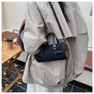 Close-up of black cylinder crossbody bag with silver hardware in a cozy cafe setting