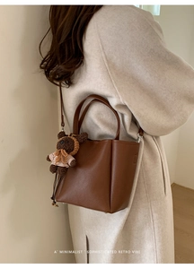 Detail of dark brown pebble leather bucket bag with a cute bear charm on autumn coat