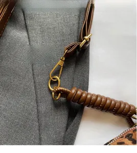 Detail of golden metal hook and braided leather handle on leopard print tote bag
