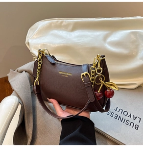 Détail de sac à main en cuir grainé marron avec chaîne dorée et breloque cerise