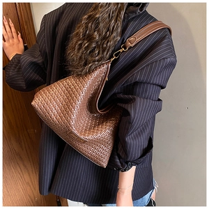 Detail of coffee woven shoulder bag with leather texture and golden metal logo plate