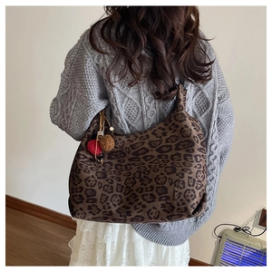 Detail of a large leopard print tote bag with plush pom-pom charms shown on shoulder