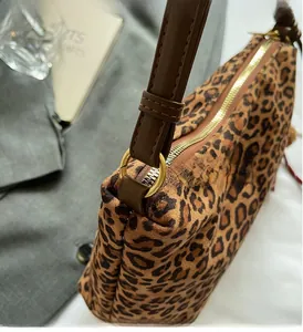 Macro detail of high-shine gold zipper and brown leather strap on leopard tote bag