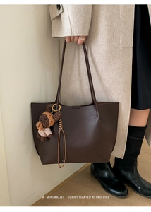 Detail of dark brown leather tote bag with a cute knitted bear charm on the shoulder strap