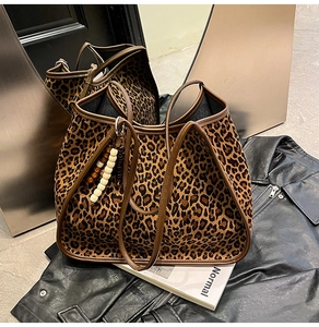 Detail of leopard print tote bag with brown leather handles and wooden bead charm accent