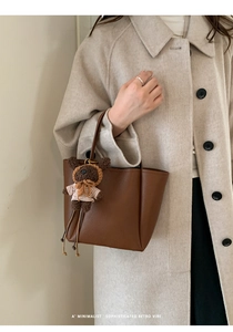 Close-up of brown litchi pattern leather bucket bag with cute plush bear charm decoration