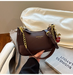 Detail of dark brown leather underarm bag with gold chain and cherry charm detail