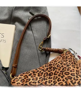 Close-up of leopard print canvas bag with brown leather strap and gold metal buckle detail