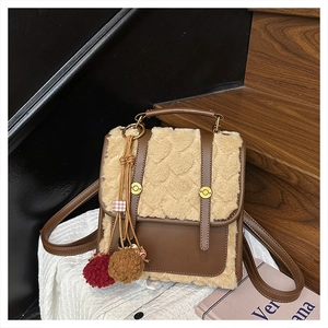 Detail of a brown leather backpack with beige plush heart-patterned accents and pompom charm