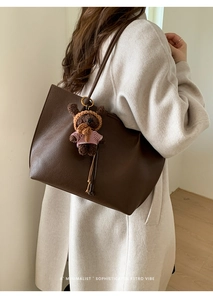 Detail of dark brown pebble leather tote bag featuring a cute plush bear charm accessory