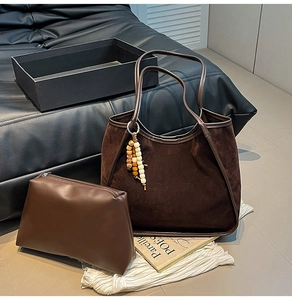Detail view of brown suede tote bag featuring leather straps and wooden bead tassel