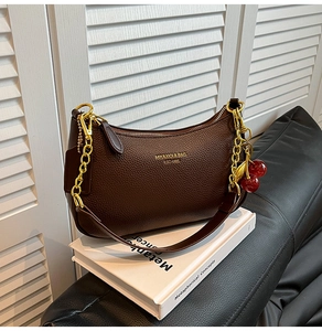 Detail of dark brown lychee leather hobo bag with gold chain and cherry pendant