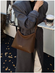 Close-up of brown woven leather hobo bag featuring metallic logo and elegant shoulder strap