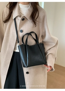 Close-up of minimalist black pebbled leather bucket bag worn as a crossbody with a coat