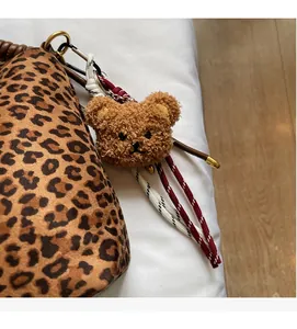 Detail of leopard print tote bag with plush bear charm and woven red white strap cord
