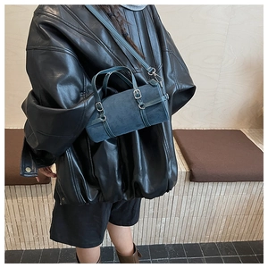 Detail of dark blue cylindrical shoulder bag with suede texture and metal buckle on model