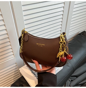 Detail of dark brown leather crescent bag with gold chain and cherry charm accessory