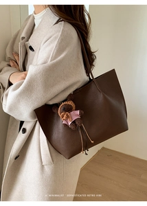 Detail view of large brown leather tote bag with retro knitted bear charm and pebble texture