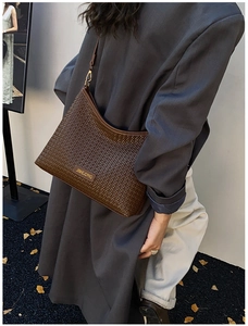 Detail of dark brown woven leather texture with gold brand plate on an underarm bag