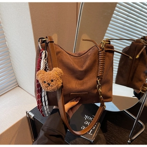 Détail d'un sac cabas en daim marron foncé avec un porte-clés ours en peluche et corde