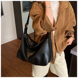Close-up of soft black leather tote bag with gold buckle on a brown casual outfit