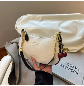 Detail of white lychee leather crescent bag with gold chain and cherry charm accessory