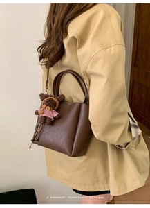 Detail of dark brown pebble leather bucket bag with a cute teddy bear charm on the side