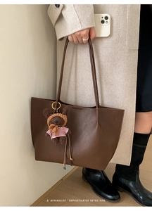 Detail of a brown lychee pattern tote bag featuring a cute teddy bear charm with shoulder straps