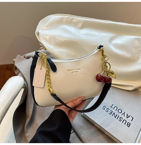 Close-up of off-white lychee leather baguette bag with gold chain and cherry charm detail