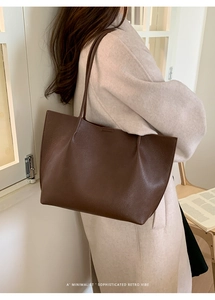 Detail view of dark brown pebbled leather tote bag worn with a beige wool coat