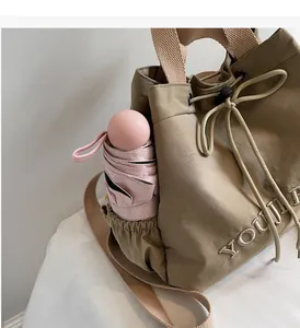 Detail view of khaki drawstring backpack with side elastic pocket holding a pink umbrella