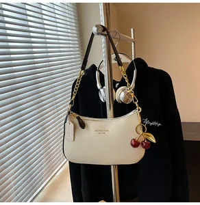 Detail of cream white leather hobo bag with gold chain strap and cherry charm accent