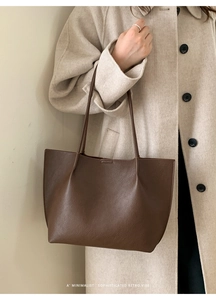 Detail of minimalist dark brown lychee leather tote bag on model in beige coat