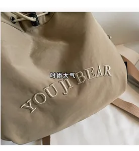 Detail of khaki drawstring backpack featuring YOU JI BEAR embroidery and nylon texture