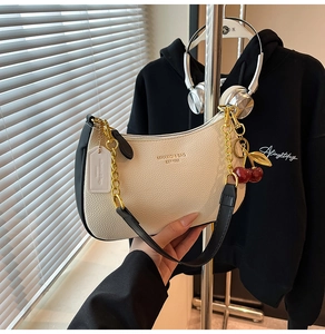 Detail of off-white crescent bag with gold chain and cherry charm in stylish lifestyle setting