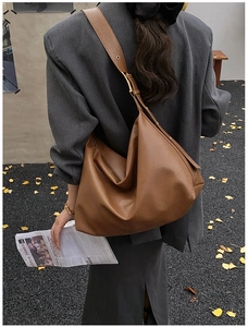 Detailed close-up of brown soft leather tote bag with gold eyelets and wide shoulder strap